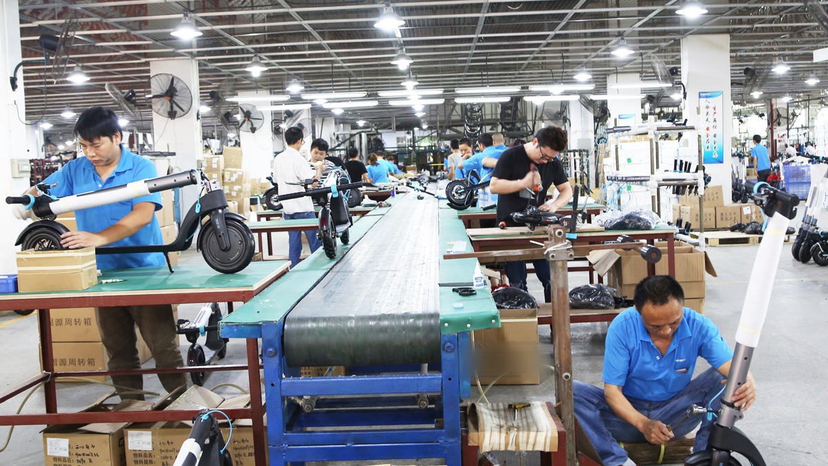 Workers in company uniform assembling electric scooters on the factory line, with export cartons staged alongside
